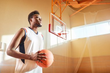 Mahkeme salonunda üzerinde duran basketbol topu tutan olumlu Afrikalı-Amerikalı adam yan görünüm. 