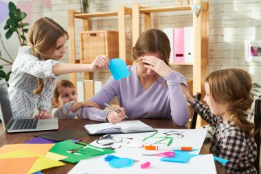 Exhausted freelance worker trying to concentrate on project while her little daughters distracting her, interior of modern living room on background clipart