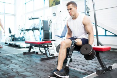 Spor salonundaki kaslı adam dambıllarla egzersiz yapıyor.