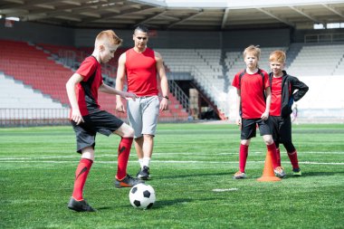 Genç futbol takımı uygulama, topu önünde onu izlerken koç ile önde gelen çocuk odaklanmak tam uzunlukta portresi