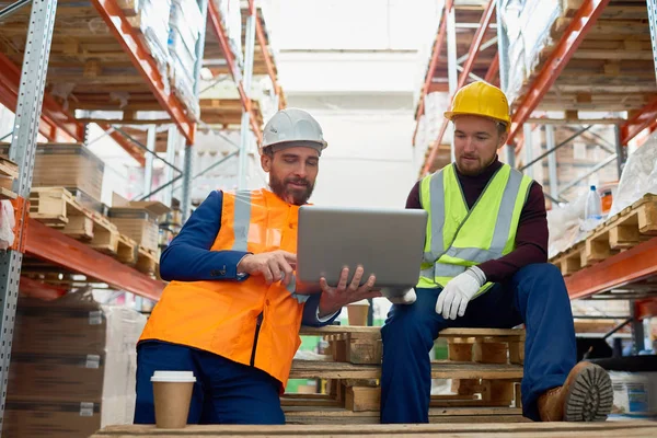 Portrait of two factory workers using laptop on break in warehouse, copy space