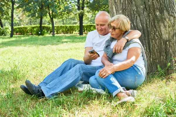 Retrato Comprimento Total Casal Sênior Moderno Sentado Sob Árvore Parque — Fotografia de Stock