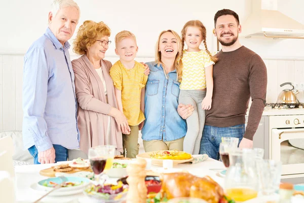 Portrait of carefree two generation family of six posing  at home and smiling   standing at festive dinner table