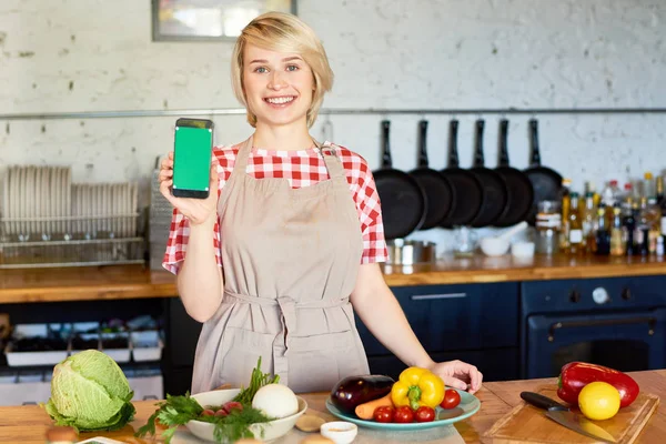 Portrait of smiling female cook showing her smartphone