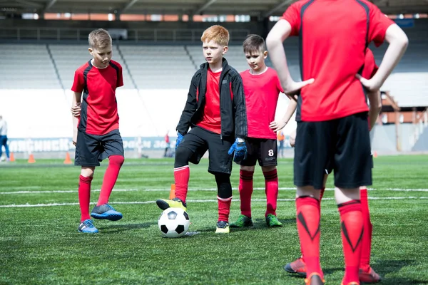 Full length portrait of junior football team practicing in stadium, focus on red haired team captain with ball, copy space