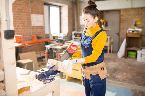 Portrait of smiling  female artisan cutting wood while working in modern furniture manufactory