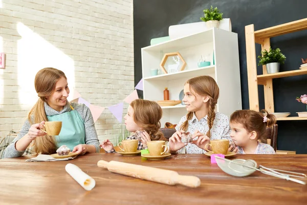 愛らしい家族は集まって一緒に家では 食欲をそそるカップケーキとお茶とおしゃべり生き生きとお互いに 背景のダイニング ルームのモダンなインテリア — ストック写真