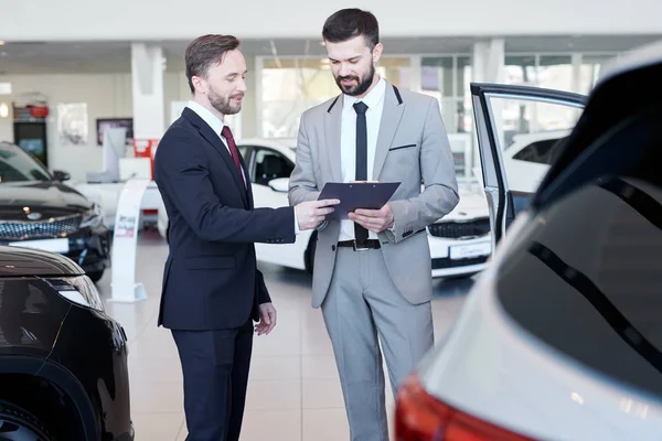 Car dealer showing a contract to the customer while standing in auto salon
