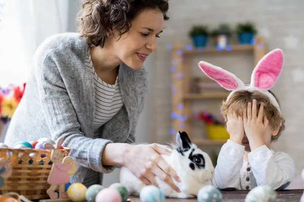 Portrait of happy young family celebrating Easter at home, mother and giving pet bunny to cute little boy with eyes closed