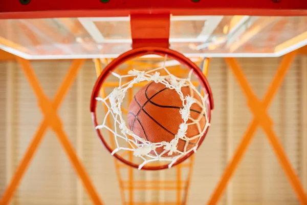 From below shot of basketball ball falling through net in gym.