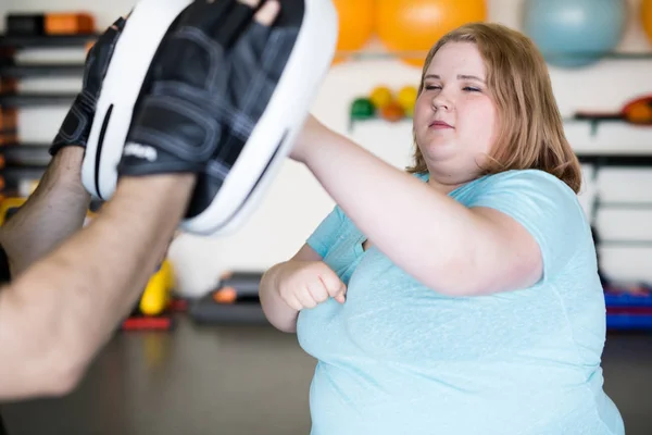 Portrait of obese young woman practicing punching during endurance training in gym