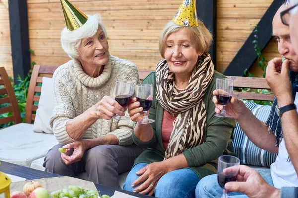 一群开朗的老年人穿着节日帽庆祝生日在户外露台与朋友 无比的酒杯和烘烤 — 图库照片