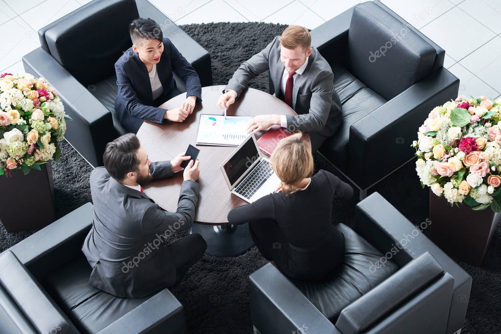 High angle view of multi-ethnic group of white collar workers gathered together at modern boardroom and analyzing results of accomplished work