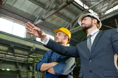 Bir şey üretim modern fabrikasında işçi ile tartışırken, uzay kopyalamak için yakışıklı işadamı işçisi işaret giyen düşük açılı portresi