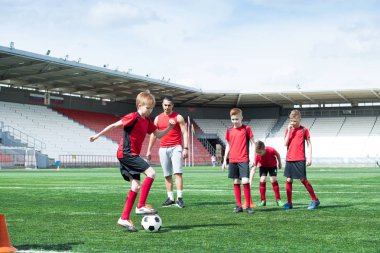 Genç futbol takımı uygulama, onu kopya alanı izlerken koç ile çocuk önde gelen topu odaklanmak tam uzunlukta portresi