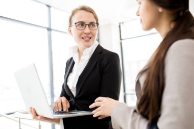 Başlangıç tartışıyor güzel genç beyaz yakalı işçiler ise geniş ofis lobisinde ayakta ve toplantı, onlardan biri holding laptop çalışma başlangıcı için bekleyen proje