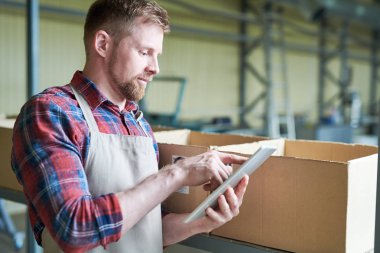 Yan görünümü dijital tablet kullanma ve kahve roastery dururken gülümseyen modern sakallı adam portresi