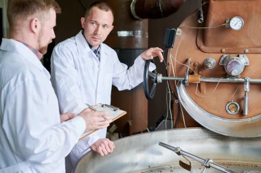 Belden yukarı iki modern genç erkek kahve roastery, kopya alanı çalışırken işleme tartışırken laboratuvar mont giyiyor portresi