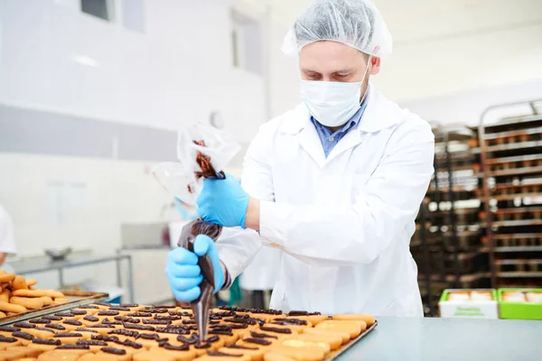 お菓子チョコレート クリームを飾るためにアイシング バッグを使用して白衣に製菓工場労働者 — ストック写真