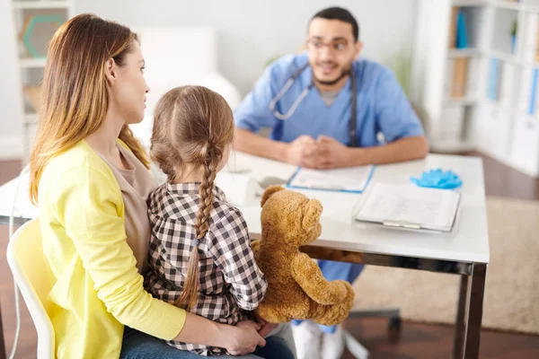 Back view portrait of young mother and little girl listening to Middle-Eastern doctor during consultation on pediatric issues, copy space