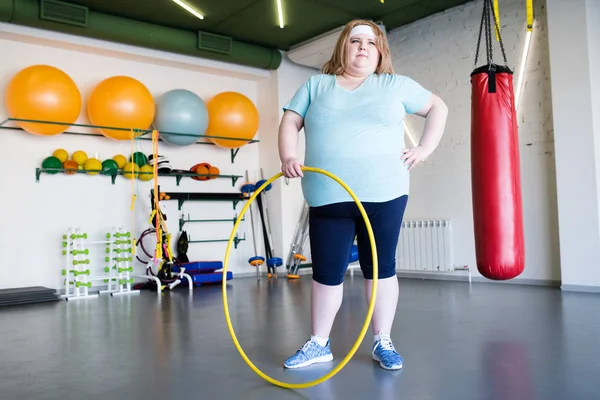 Full length portrait of  obese young woman posing with hula hoop  during weight loss training in gym
