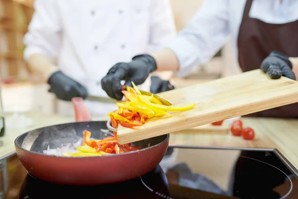 モダンなレストラン キッチン コピー領域の手袋をはめた手でフライパンに食材を入れてモダンなプロのシェフのクローズ アップ — ストック写真