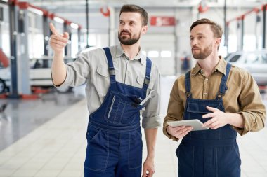 Atölye yürüyüş ve uzak araba bakım ve onarım merkezi çalışırken gösteren iki modern sakallı mekaniği portresi kadar bel