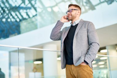 Proje detayları Smartphone cep telefonu ile modern ofis lobisinde dururken meslektaşı ile tartışırken sakallı Yöneticisi giyen şık giysiler gülümseyen