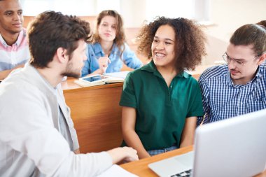 Neşeli heyecanlı çok ırklı grup Üniversitesi Danışma reklam sınıf içinde laptop raporu hazırlarken proje tartışıyor, oturmak