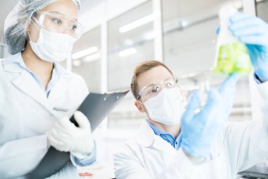 Tıbbi araştırma yeşil sıvı kabı içinde laboratuvar masasında otururken eğitim üzerinde çalışan iki modern bilim adamları portresi