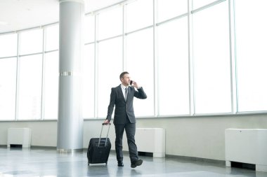 Bavul taşıma ve telefonla konuşma modern Havaalanı salonu genelinde yürüyüş başarılı iş adamı tam uzunlukta portresi