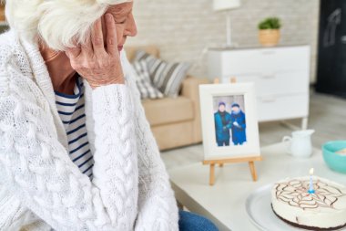 Baş taraftan yaslanmış ve düşünceli pastaya bir mum fotoğraf ile geçmiş hatırlama kocası ile görünümlü ve yumuşak hırka üzücü yalnız yaşlı kadın