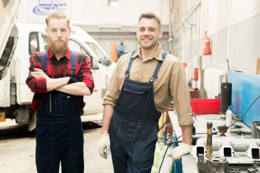 Hizmet garajda duran ve kameraya bakarak Üniformalı Genç beyaz erkek araba mekaniği portresi