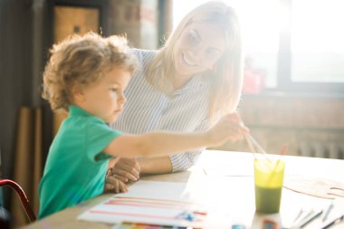 Sıcak tonlu yan görünümü Sunlight Genç Anne ya da öğretmen ile masada oturan sevimli küçük çocuk başındaki resimleri portresi
