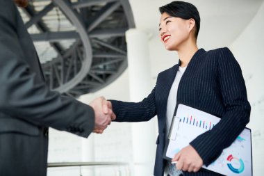 Onun iş ortağı ona el sıkışma, office lobi iç arka plan ile tebrik ederken çekici gülümseme ile bakarak resmi kıyafeti içinde gülümseyen Asya girişimci düşük açılı görünüş
