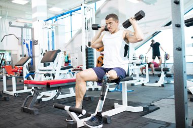 Protez bacak modern bir spor salonu bankta oturmuş dumbbells ile çalışma dışarı ile yakışıklı kaslı adam portresi tam uzunlukta