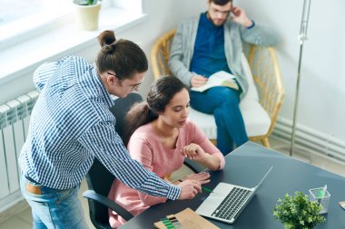 Proje açıklayan ve Toplantı salonunun içinde laptop doğru verileri için İspanyol kadın uzmanı soran emin genç tasarımcı