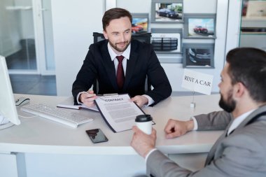 Kendine güvenen satıcı müşteri ile masada çalışan takım elbiseli. O rent a car sözleşmenin koşulları gösteriyor