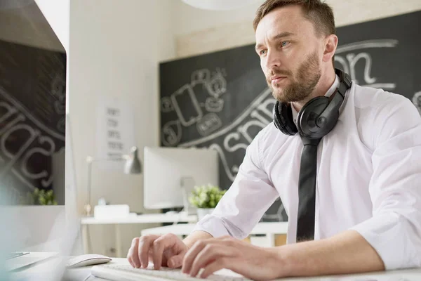 잘생긴 수염된 실업가 셔츠와 컴퓨터를 사무실에서 책상에 넥타이 헤드폰 입력의 — 스톡 사진