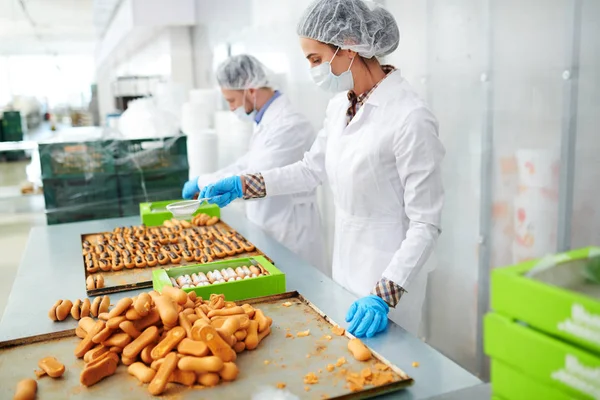 Confectionery factory workers in white coats standing and preparing delicious pastry.