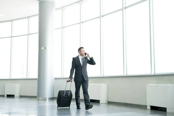 成功商人穿越现代机场大厅的全长肖像携带手提箱和电话通话 — 图库照片