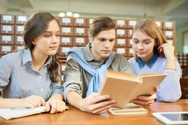 Serios Amigos Estudiantes Inquisitivos Leyendo Libro Juntos Sentados Mesa Mientras — Foto de Stock