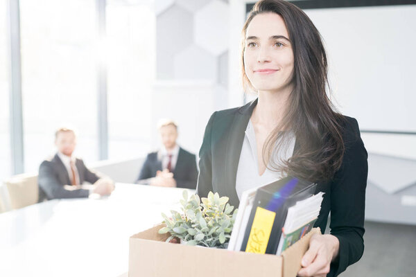 Waist up portrait of smiling young businesswoman holding box of personal belongings leaving office after quitting job 