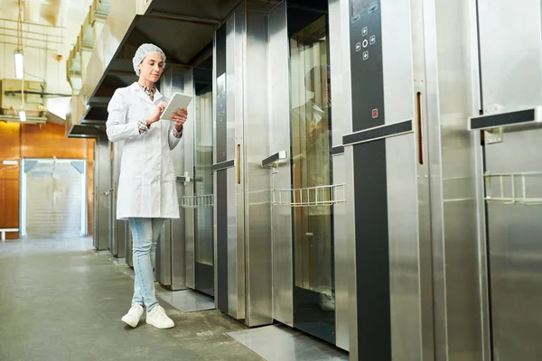 エレベーターの近くに立って タブレット コンピューターを使用して白衣に製菓工場従業員 — ストック写真