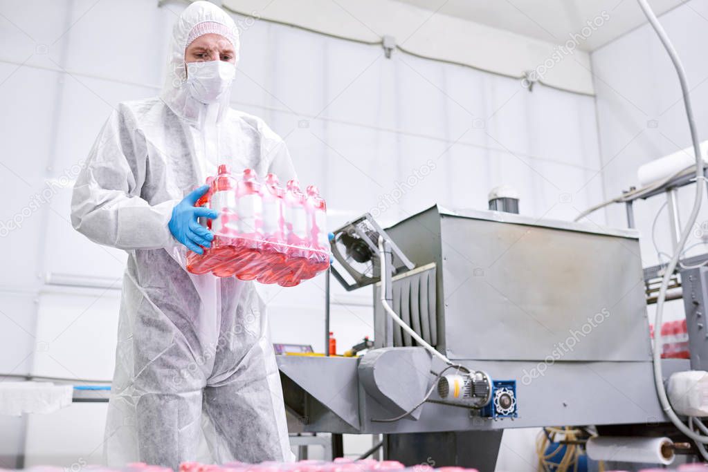 Sports nutrition production worker in protective clothing carrying ready pack of plastic bottles with drink.