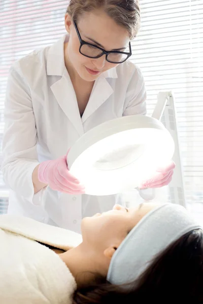 Concentrated Young Cosmetologist Wearing Eyeglasses White Coat Looking Magnifying Lamp — Stock Photo, Image