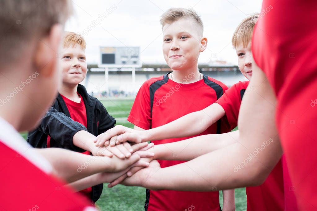 Portrait of junior football team stacking hands during motivational pep talk before match in outdoor stadium, copy space