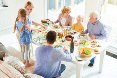 High angle portrait of happy two generation  family enjoying dinner together sitting at festive table with delicious dishes during  holiday  celebration in modern sunlit apartment, copy space clipart