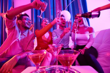 Mutlu bir şekilde gülerek garson dökme şampanya kanepede oturan, özel parti zevk çekici insanların gözlük flüt grup portresi düşük açılı