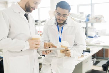 Ciddi konsantre yakışıklı çok ırklı mühendisler laboratuvar kat süre tablete verileri görüntüleme ve cihaz üretimi fabrika Office tartışırken kahve içme olarak